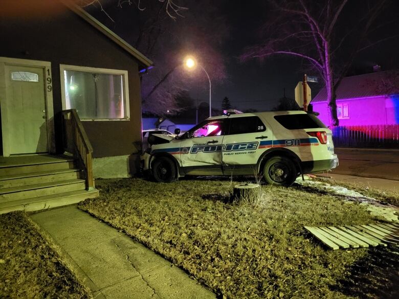 The police car is resting on the lawn of the home it hit and damage on it's side and the hood can be seen