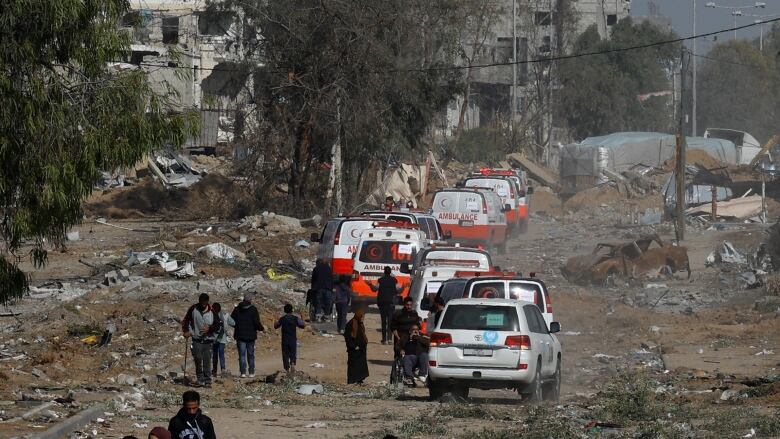 A trail of ambulances surrounded by people. 