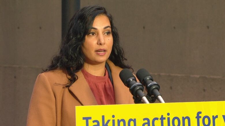 Nikki Sharma speaks into a microphone at a podium outside.