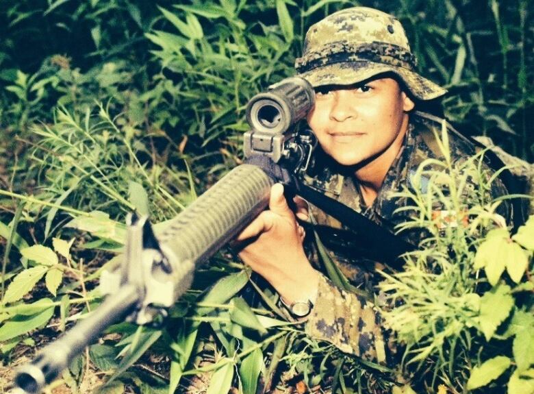 A woman in a military uniform holds a gun.