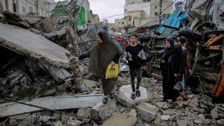 People walk amid the debris of destroyed buildings.