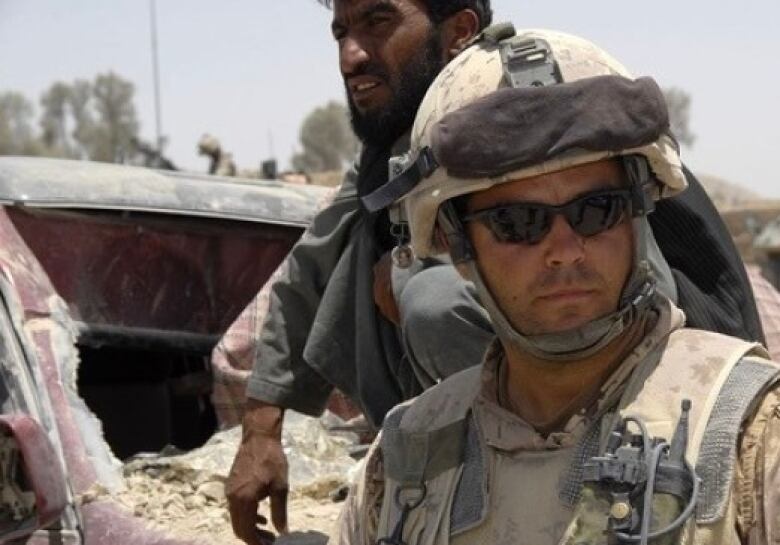 A man poses, wearing a helmet in a military uniform.