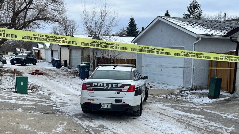 A police car is seen in a snowy back lane, with police tape across the alley