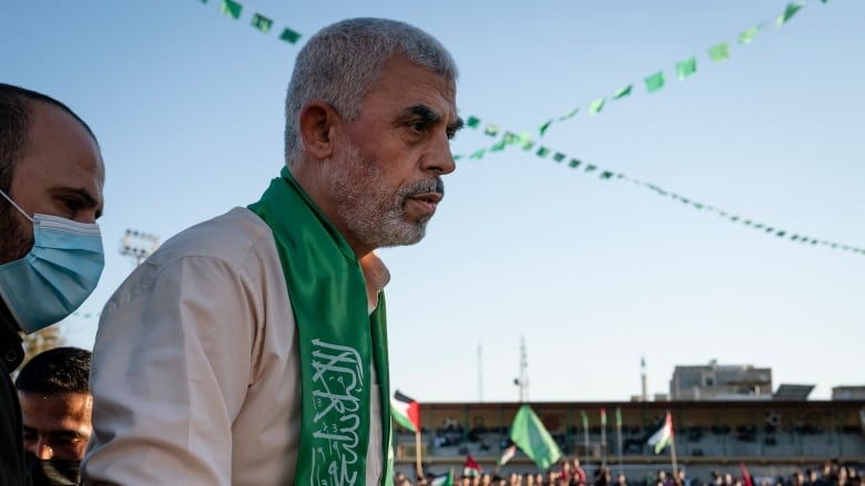 A Hamas political leader on stage with supporters waving Palestinian flags in the background.