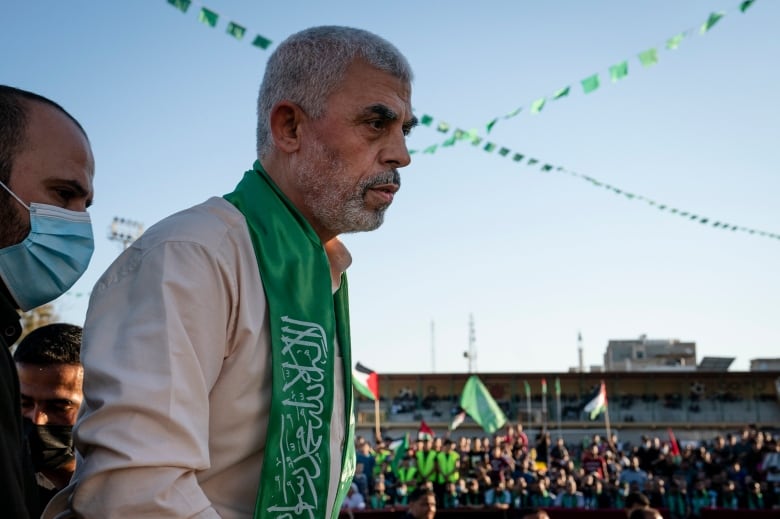 A Hamas political leader on stage with supporters waving Palestinian flags in the background.