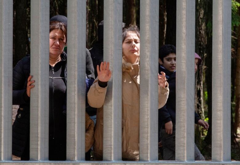 Women and children behind a large metal border fence. 