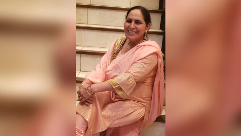 A South Asian woman wearing pink poses while seated on stairs.