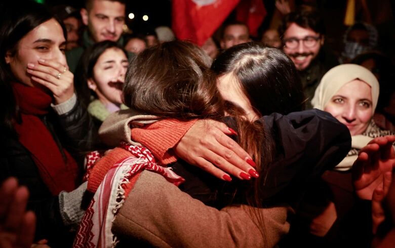 Two people hug while a happy crowd around them looks on.