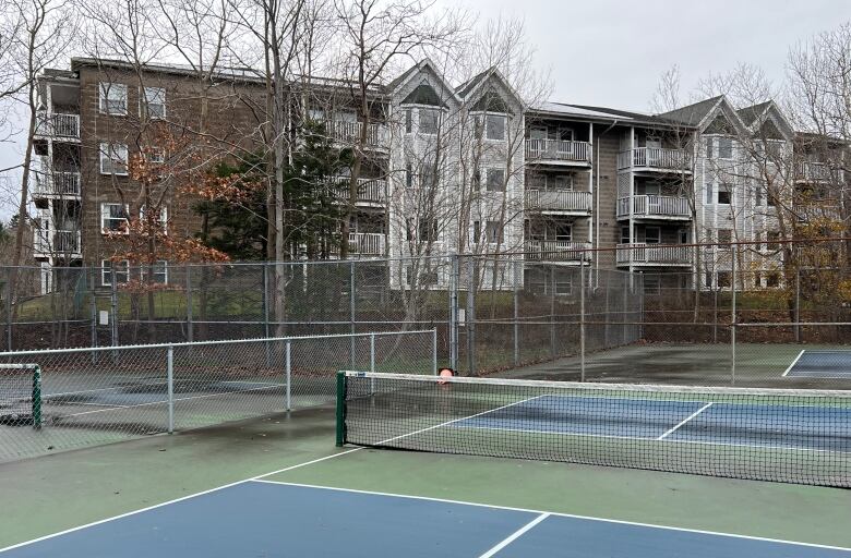 A fenced-in area with a green and blue floor, painted with white lines, and a low-rise building in the background.