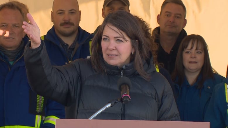 Lady in a black jacket speaking at a podium 