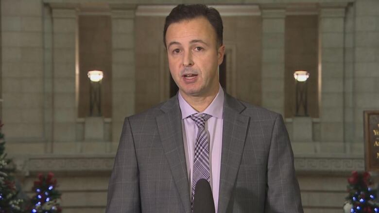 A man in a suit is pictured speaking at a podium.