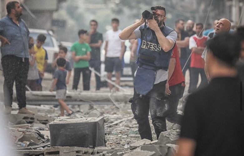 Man standing on top of rubble looking into a camera. 