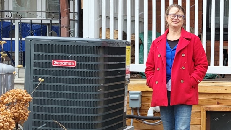 Woman stands beside a heat pump fan.