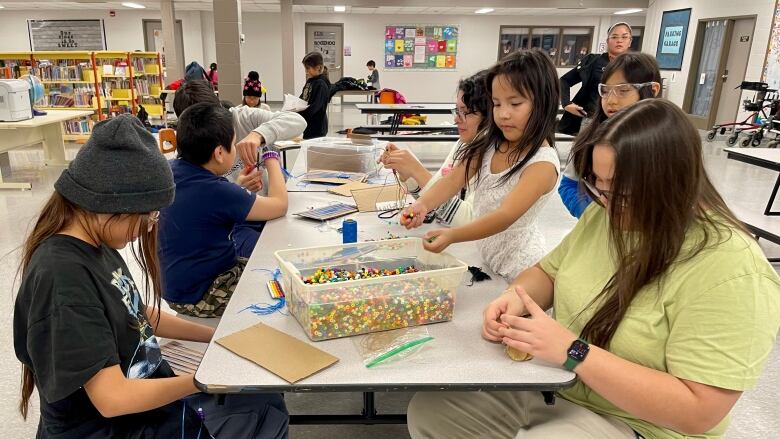 students sit together around a table working on wampum belts with a bin of beads in the middle