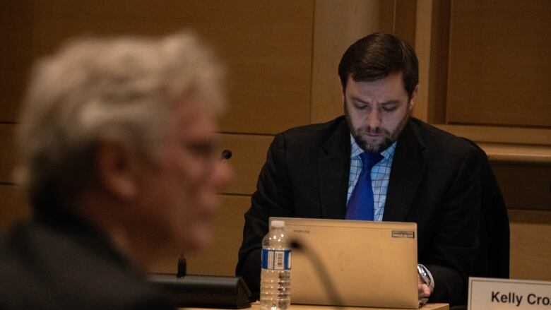 A man in a suit looks down while listening to a man with white hair