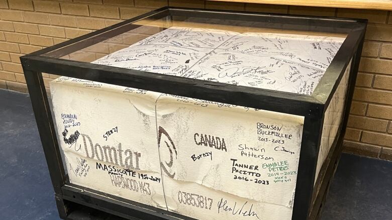 A bale placed in a glass box signed by people who worked at the mill.