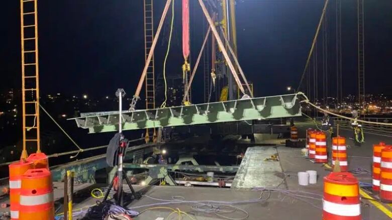 A panel on a bridge is raised by a crane. It's surrounded by safety pylons. 