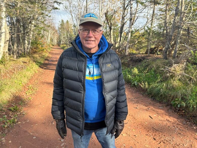 A man in a wintry coat with a blue sweater standing on a red dirt road in Prince Edward Island.