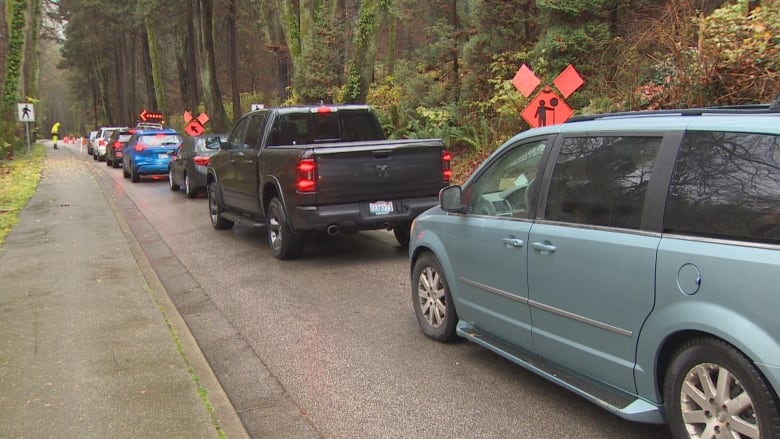 A row of cars waiting on a road in a forested area with construction ahead.