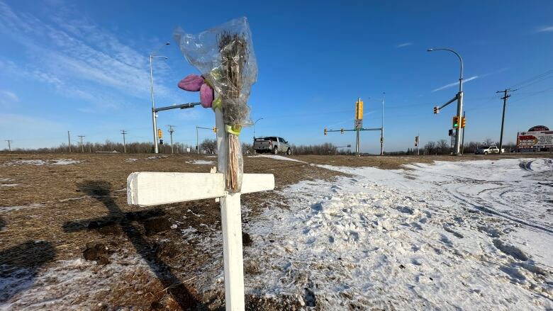 A white cross with flowers on it sits near an intersection.