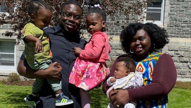 A Black couple pose with their three children in front of a stone building.