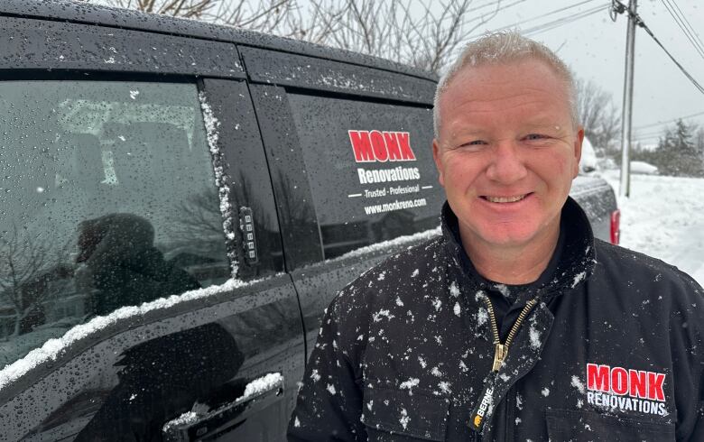 A man wearing a black jacket standing next to a black truck.