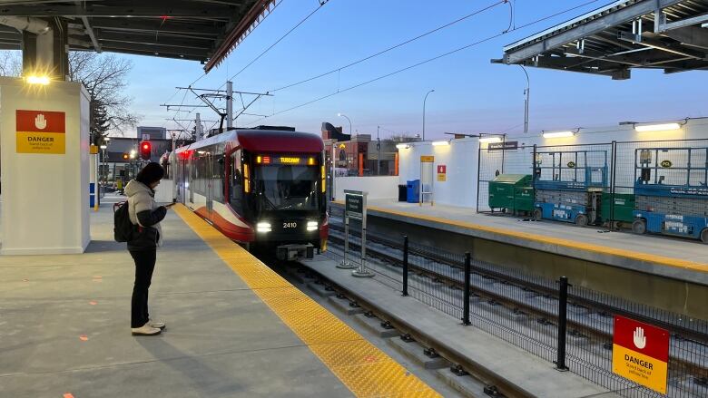 A woman stands alone on a CTrain platform as a train arrives.