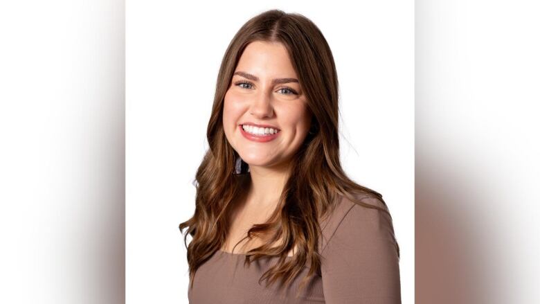 A young woman smiles for a posed photo in front of a white backdrop.