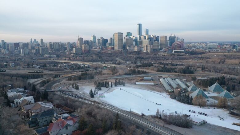 Aerial drone footage of a snowy field and dead green grass among a city skyline