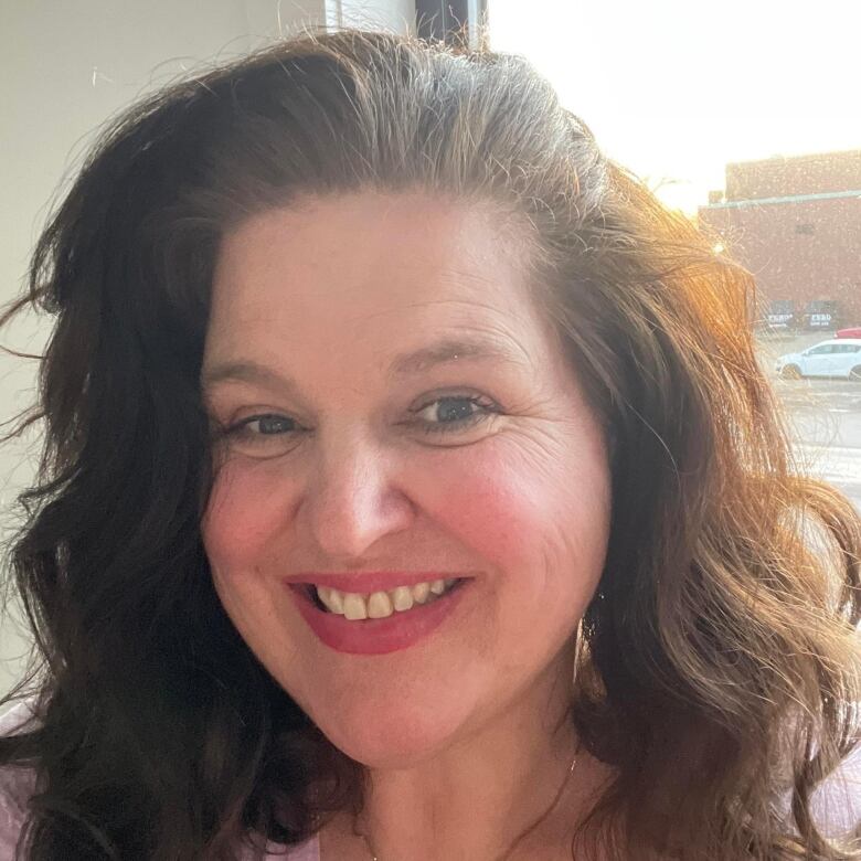 A smiling woman with wavy brown hair, wearing pink lipstick.