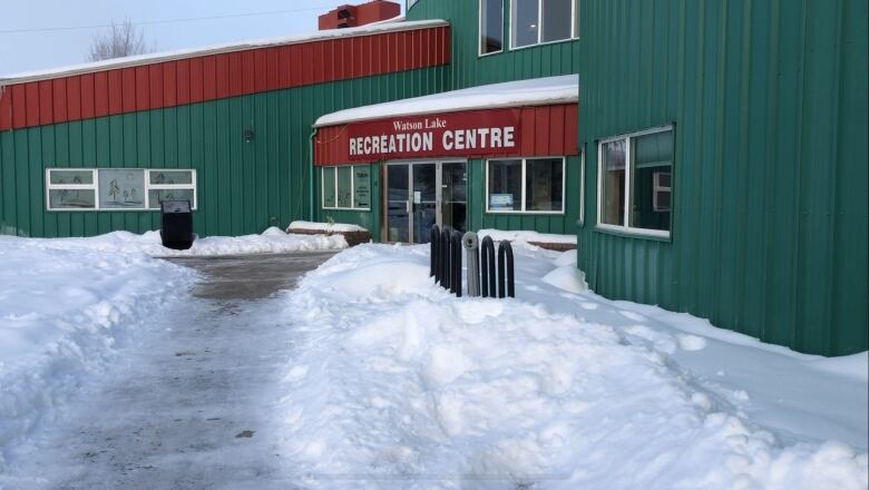 The entrance to a large green building with a snowy sidewalk.