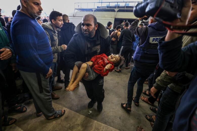 An injured child is carried through a crowd by an adult.