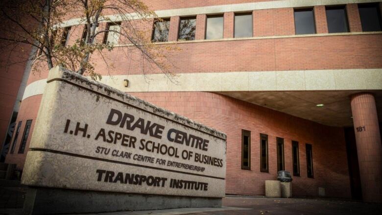 A concrete slab with a sign for Drake Centre, Asper School of Business at University of Manitoba is seen in the foreground with a building in the background.