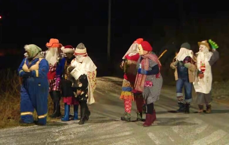 A group of mummers walk down a road at night time.