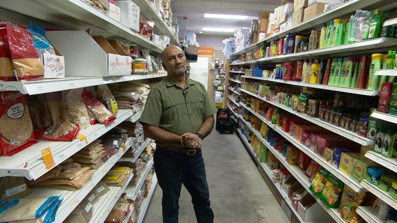 A man can be seen wearing a green shirt and black pants, he is standing between the aisles of a grocery store. 