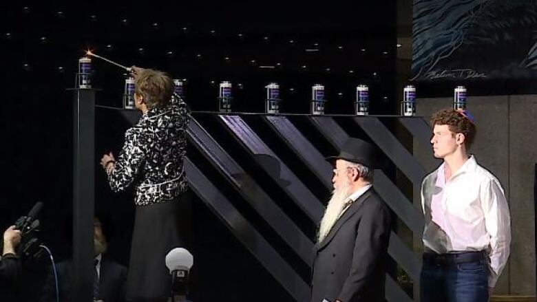 A woman stands on a ladder to light a Menorah. 