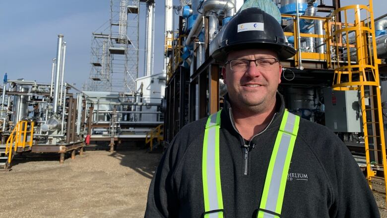 A man in a hard hat, black fleece and high-visibility vest is pictured outside a helium purification plant in Alberta.