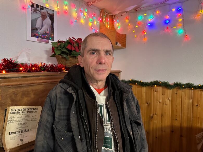 An older man stands in a room decorated with Christmas lights.