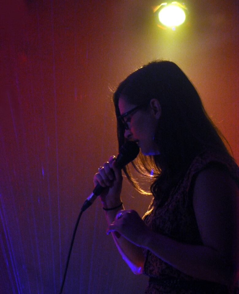 A silhouette of a woman singing into a microphone with a spotlight shining behind her.