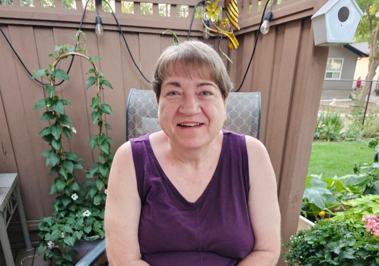 A woman in a purple tank top sits by a cake with the number 59 on it. 