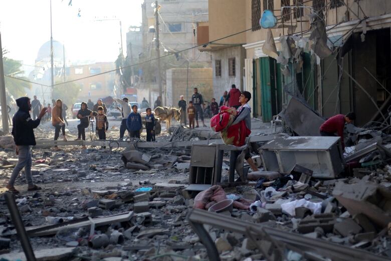 A boy carries several items amid the rubble of a building.