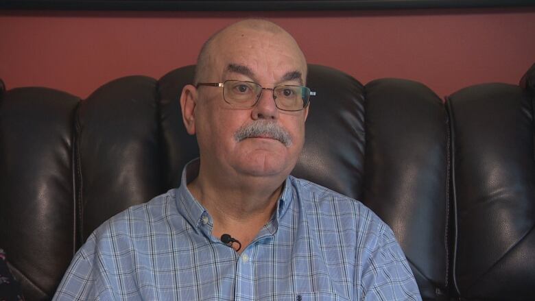 A man in a blue button-up shirt sits on a black couch.