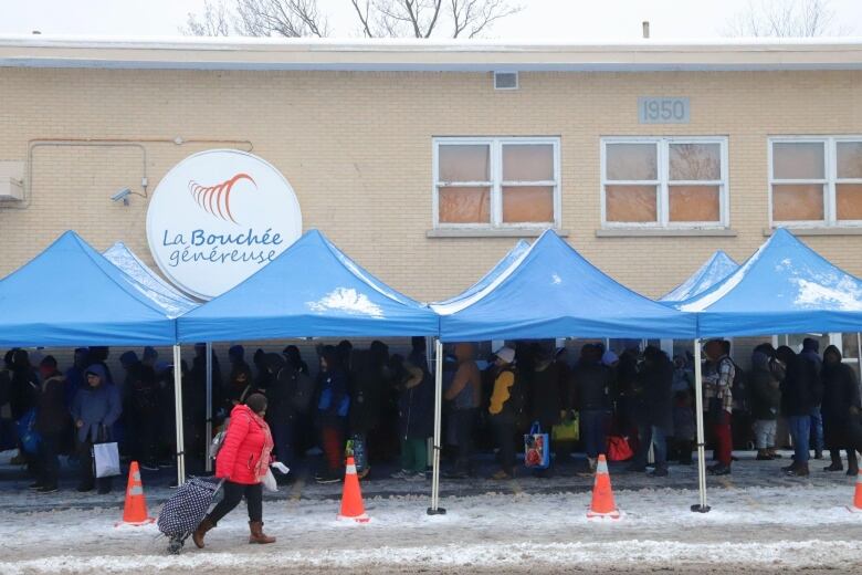 Blue plastic tents cover people waiting in line outside of a foodbank