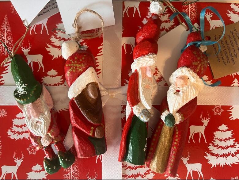 Four wooden Santa ornaments, standing about 15 centimetres each and hand-painted red, white and green, sit on top of what looks like a red holiday gift box with images of white trees and deer on it.