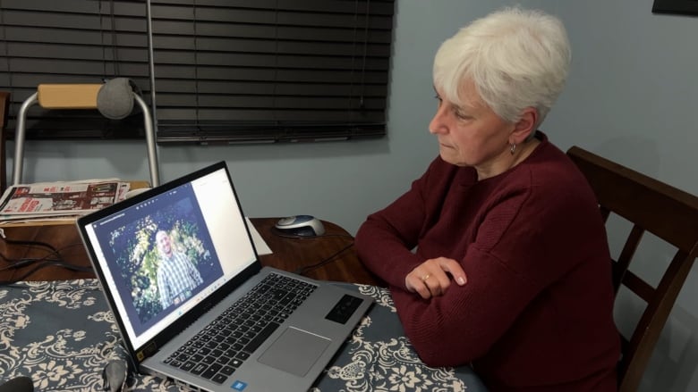 Middle aged mother Alison peace looks solemnly at a photo of her son Michael on a laptop in front of her while sitting at her kitchen table. 