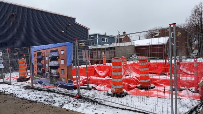 A construction site with a mock-up of a building displayed on a chain fence.