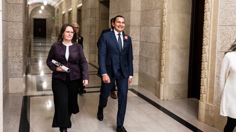 A man and two women walk through a stone hallway