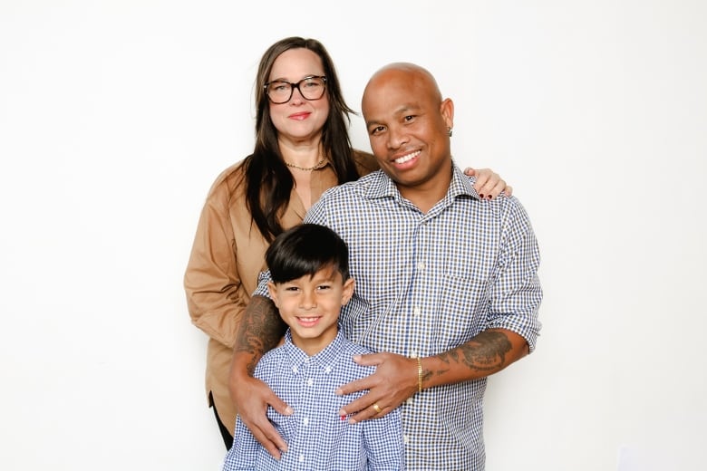 A woman stands behind a man with his arms around a boys shoulders as they all pose for the camera and smile.