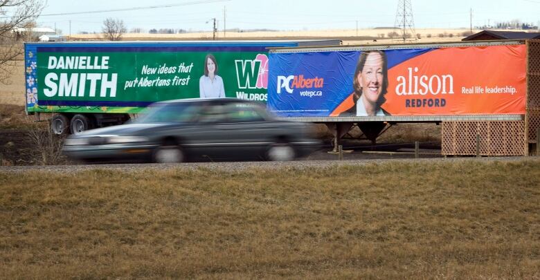 competing political billboards on the side of truck trailers on the side of  a road.