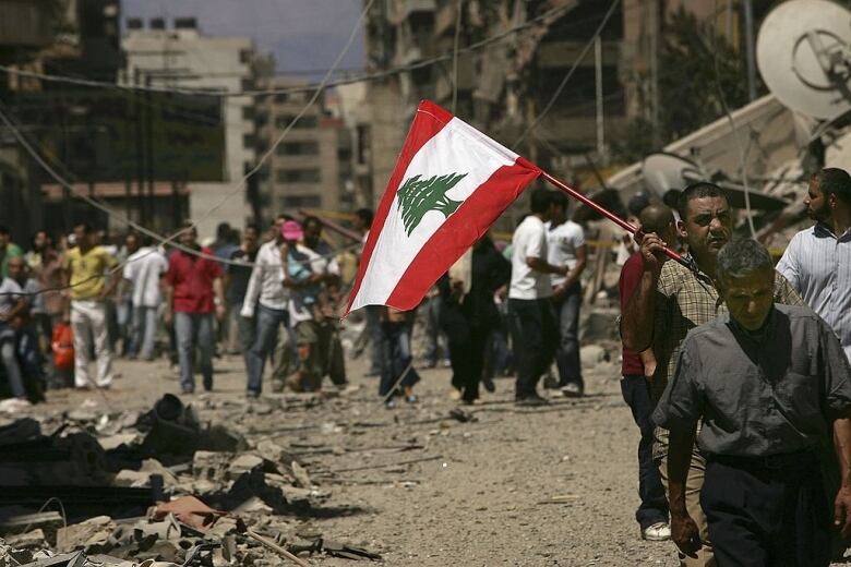 BEIRUT, LEBANON - AUGUST 14: Holding a Lebanese flag, Lebanese people returned to the southern suburbs to check on homes and businesses and to view the damage from Israeli air attacks to the area on August 14, 2006 in Beirut, Lebanon. After a U.N. brokered ceasefire came into effect between Israel and the militant group Hezbollah, Lebanese have been streaming south by the thousands.  (Photo by Spencer Platt/Getty Images)